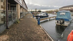 A canal with boats docked, a brick pathway, and buildings with large windows. - 6 Swan House (Carnforth)