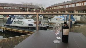 A table with a bottle of wine and a glass, overlooking a canal with boats and buildings in the background. - 6 Swan House (Carnforth)