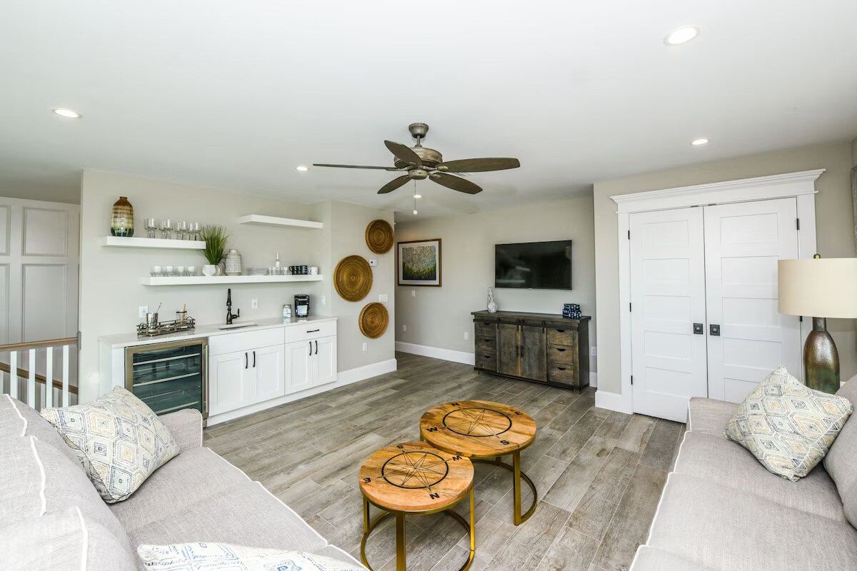 A modern living room with a sofa, two round tables, a ceiling fan, and a kitchen area with cabinets and a TV.