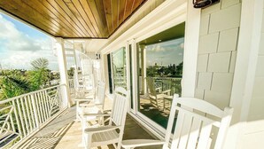 A covered outdoor area with white chairs and tables, a wooden ceiling, and large windows offering a view of the landscape. - Luxury Home with Pool, Spa and Rooftop! (Holmes Beach)