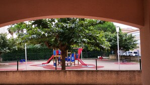 A playground with a red slide and climbing structures, surrounded by a fence and trees. - Studio RDC Grau d'Agde 100m from the beach (Agde)