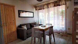 A living room with a sofa, a dining table with chairs, a wooden wardrobe, and a mirror on the wall. - Studio RDC Grau d'Agde 100m from the beach (Agde)