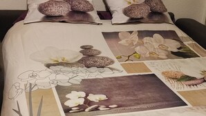 A bed with a floral and nature-themed duvet cover, featuring images of orchids and stones. - Studio RDC Grau d'Agde 100m from the beach (Agde)