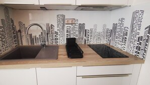 A kitchen with a double sink, a black electric kettle, and a backsplash with a cityscape design. - Studio RDC Grau d'Agde 100m from the beach (Agde)