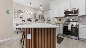A modern kitchen with white cabinets, stainless steel appliances, and a central island. - 5BR 5BA Paradiso Grande - Walk to Seaworld 10507 (Orlando)