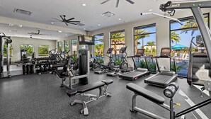 A modern gym with various exercise equipment, large windows with a view of palm trees, and ceiling fans. - 5BR 5BA Paradiso Grande - Walk to Seaworld 10507 (Orlando)