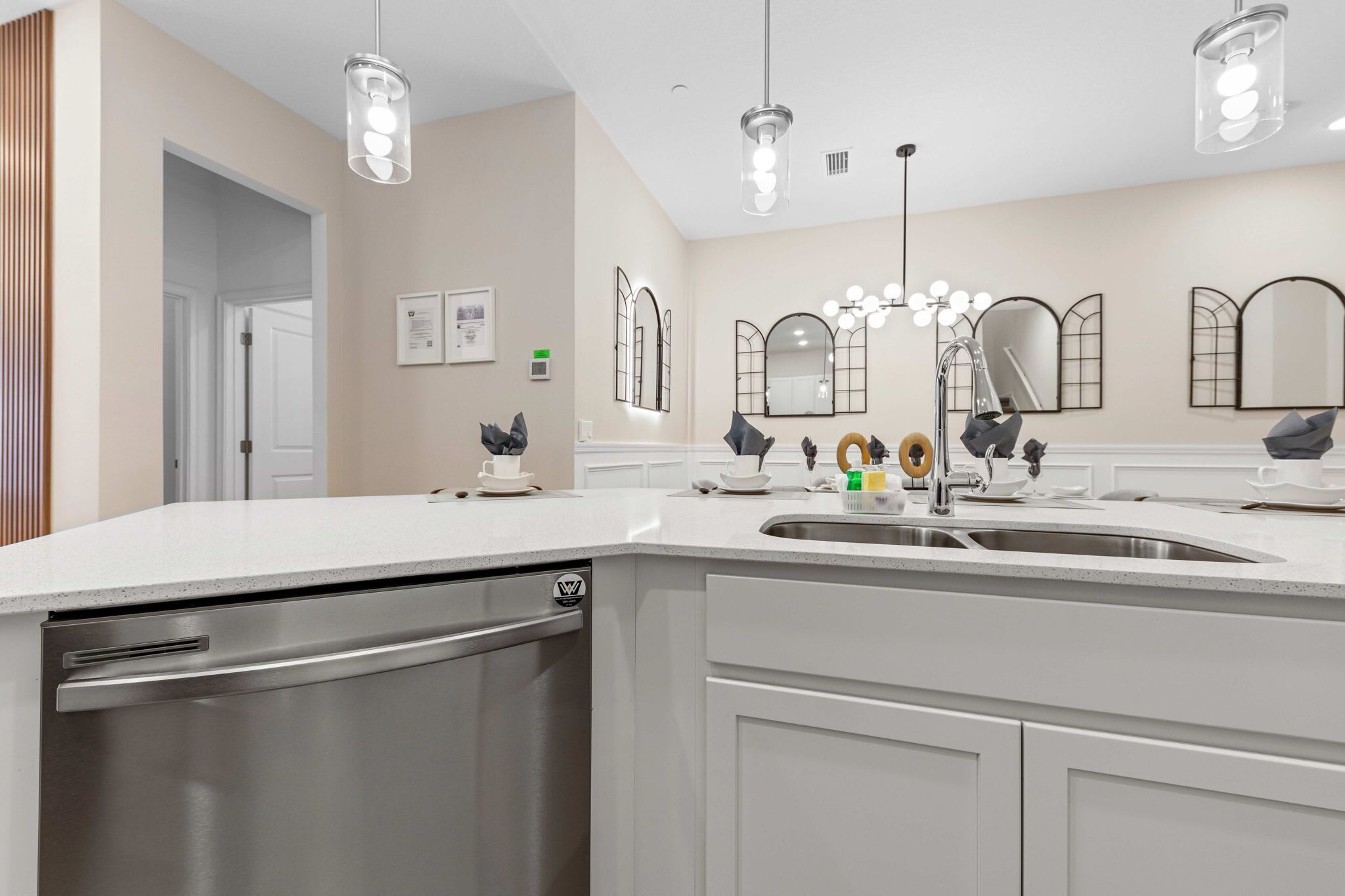 A modern kitchen with a stainless steel dishwasher, white countertops, and a large sink.