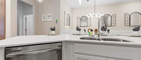 A modern kitchen with a stainless steel dishwasher, white countertops, and a large sink.