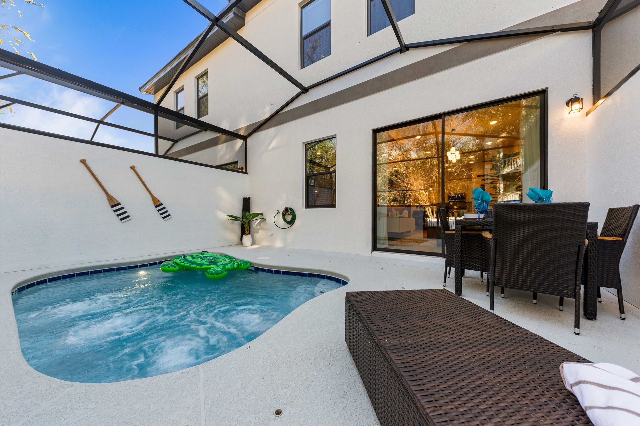 Un espace bien-être comprenant un jacuzzi, des meubles en osier et une pièce fermée par des baies vitrées, avec une table à manger.