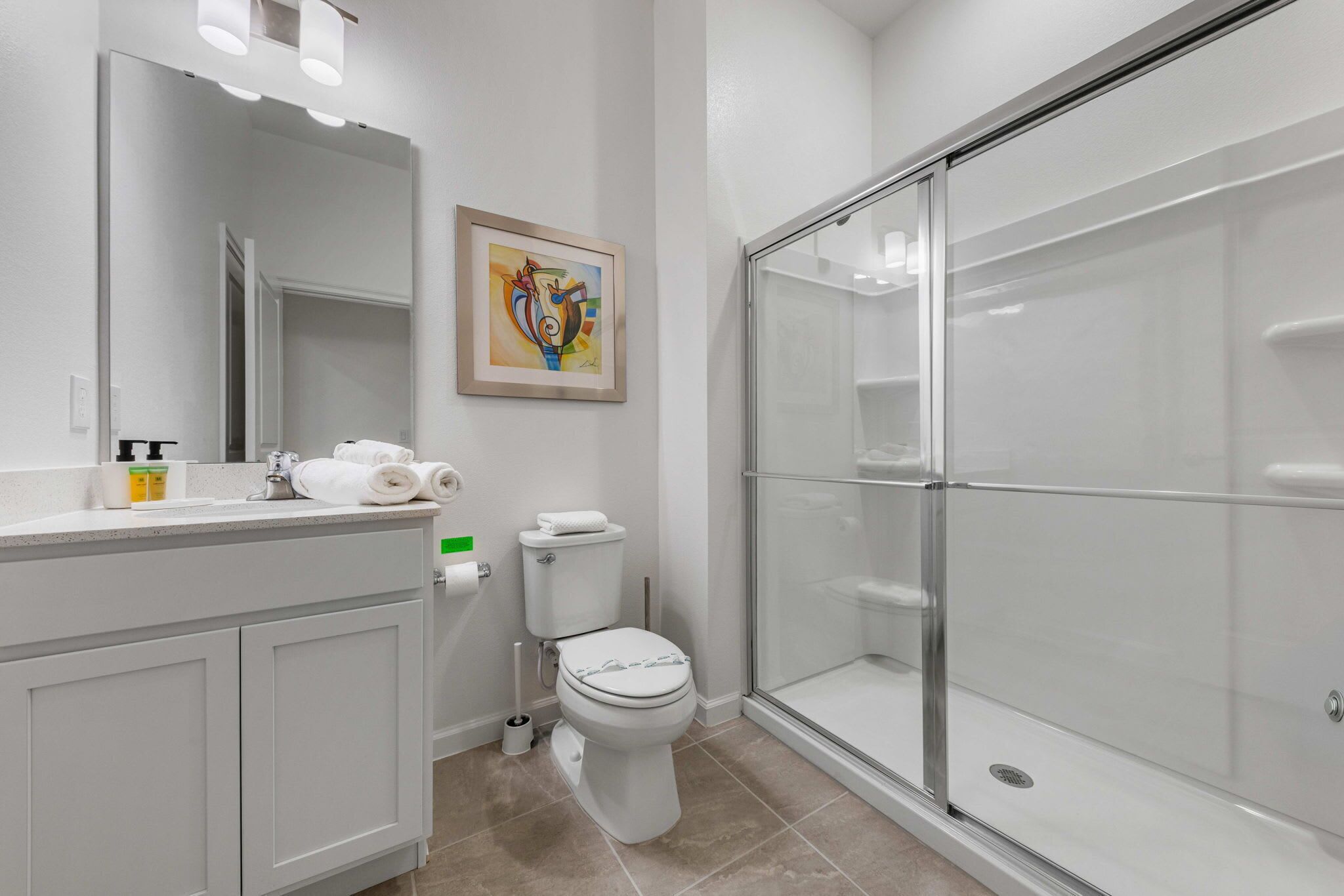 A modern bathroom with a glass shower enclosure, a toilet, and a vanity with a mirror and towel rack.