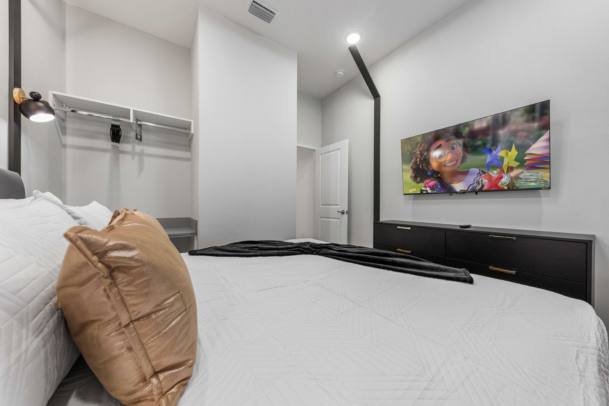 Een moderne slaapkamer met een groot bed, een televisie aan de muur en een nachtkastje.