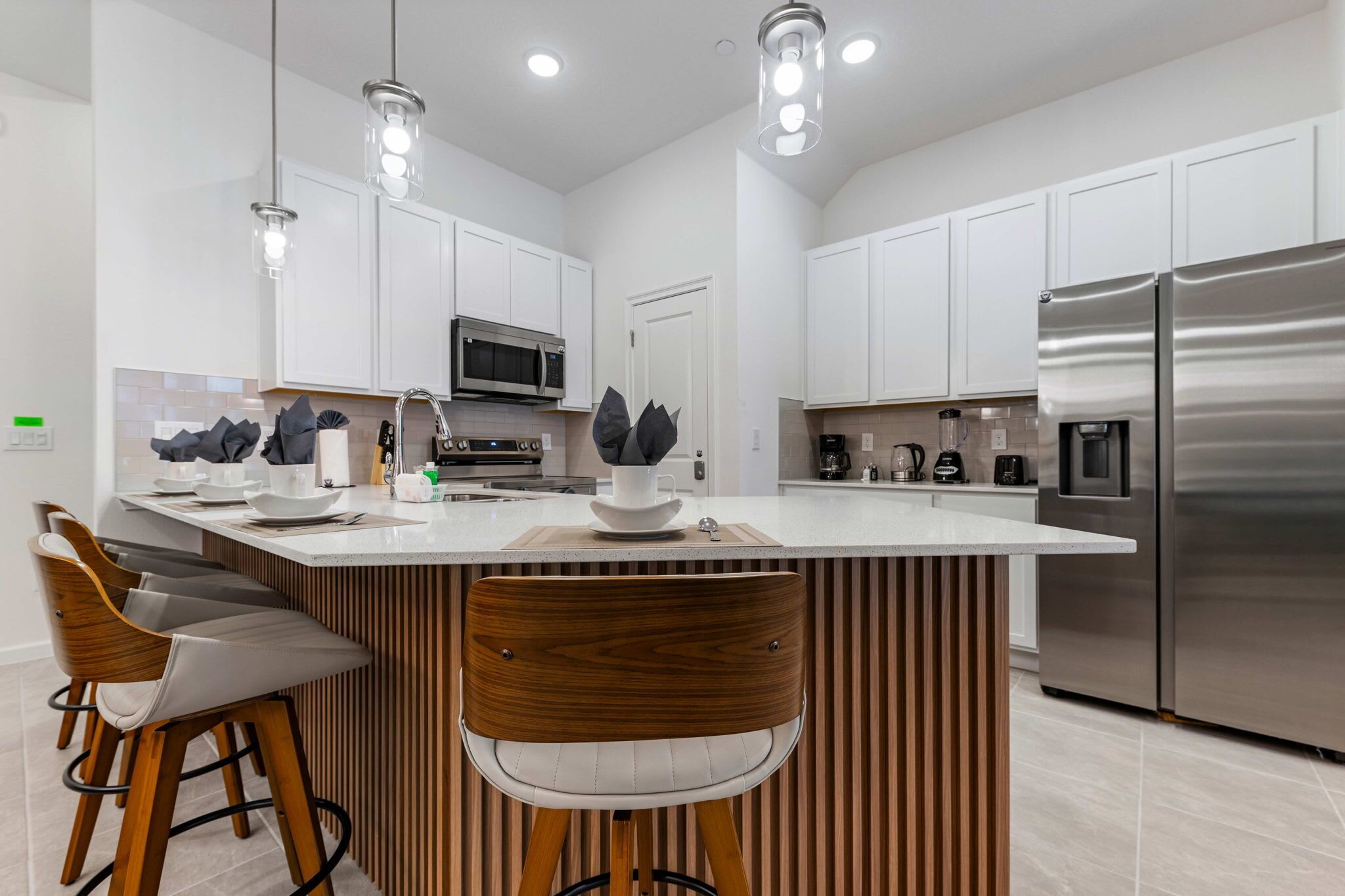 Una cocina moderna con armarios blancos, electrodomésticos de acero inoxidable y una isla central con taburetes de bar.