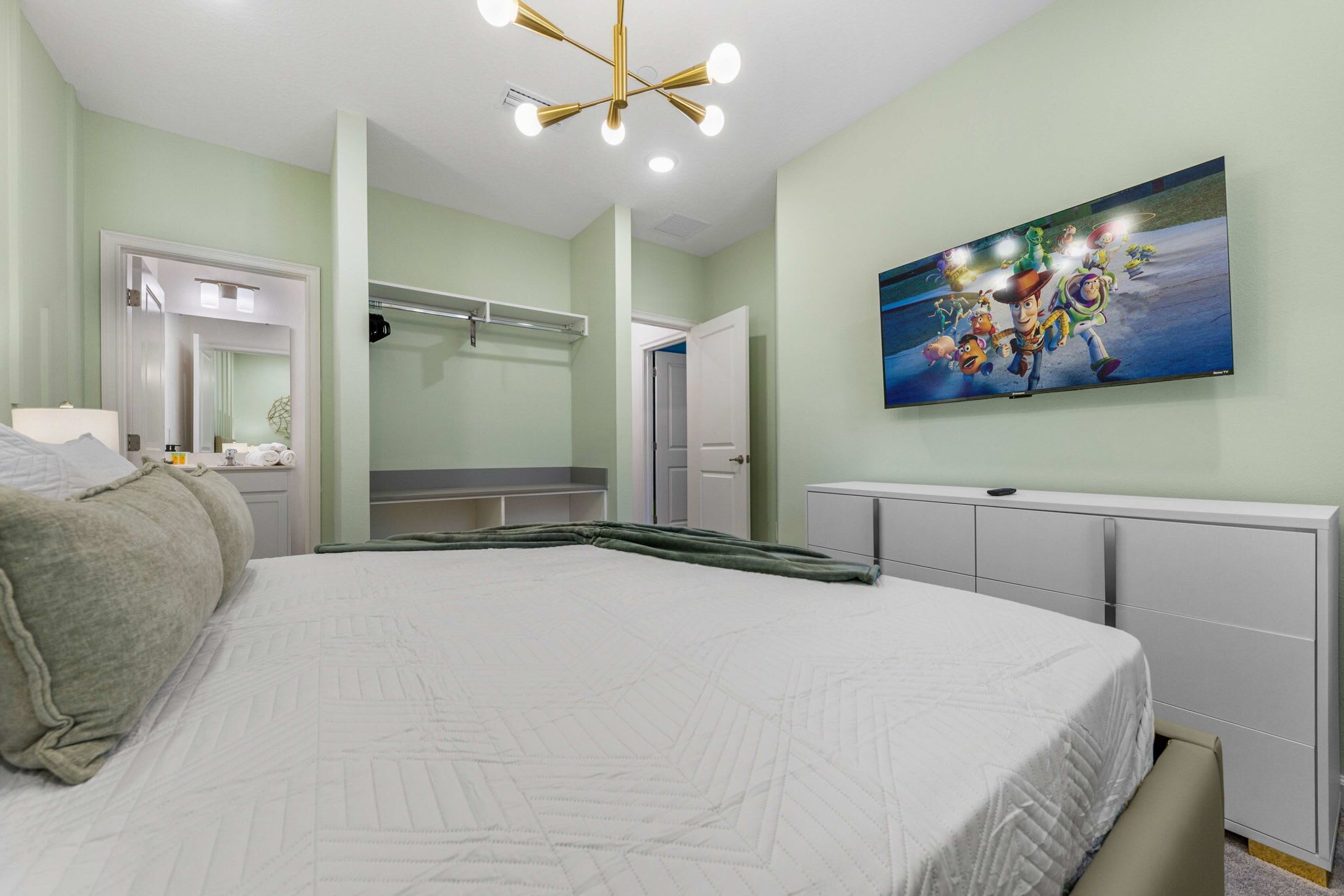 A bedroom with a large bed, a dresser, a mirror, and a painting of animated characters on the wall.