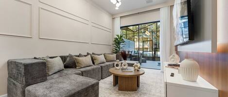 A modern living room with a sectional sofa, a round coffee table, and a flat-screen TV mounted on the wall.