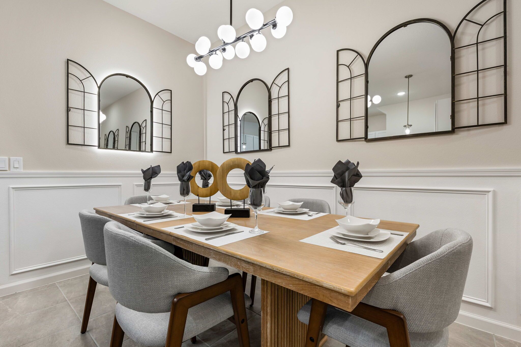 A dining area with a long wooden table, grey upholstered chairs, and decorative wall mirrors.
