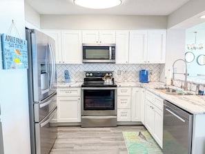 A modern kitchen with white cabinets, stainless steel appliances, and a tiled backsplash. - Windy Hill Dunes 205 (North Myrtle Beach)
