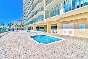 A hotel pool area with multiple pools, a covered parking area, and a building with balconies. - Windy Hill Dunes 205 (North Myrtle Beach)