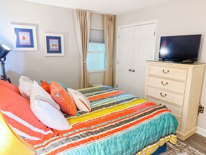 Une chambre à coucher avec un lit, un téléviseur posé sur une commode et une fenêtre avec des rideaux.