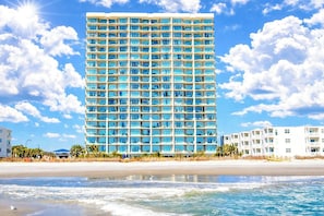 A high-rise hotel with multiple balconies, located near a beach with a clear sky. - Windy Hill Dunes 205 (North Myrtle Beach)