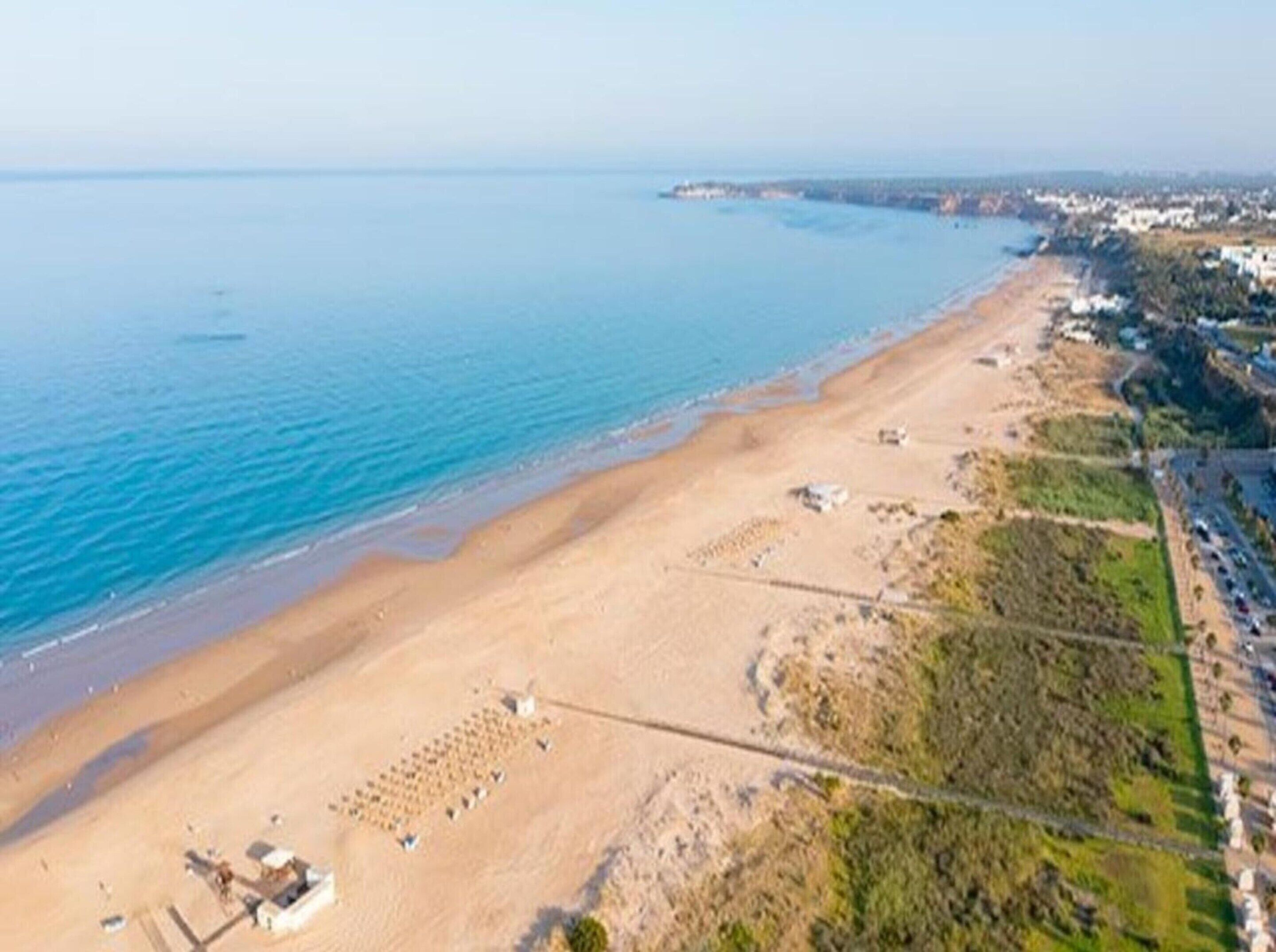 Vista aérea de una playa con orilla arenosa, algunos edificios dispersos y un mar azul y transparente.
