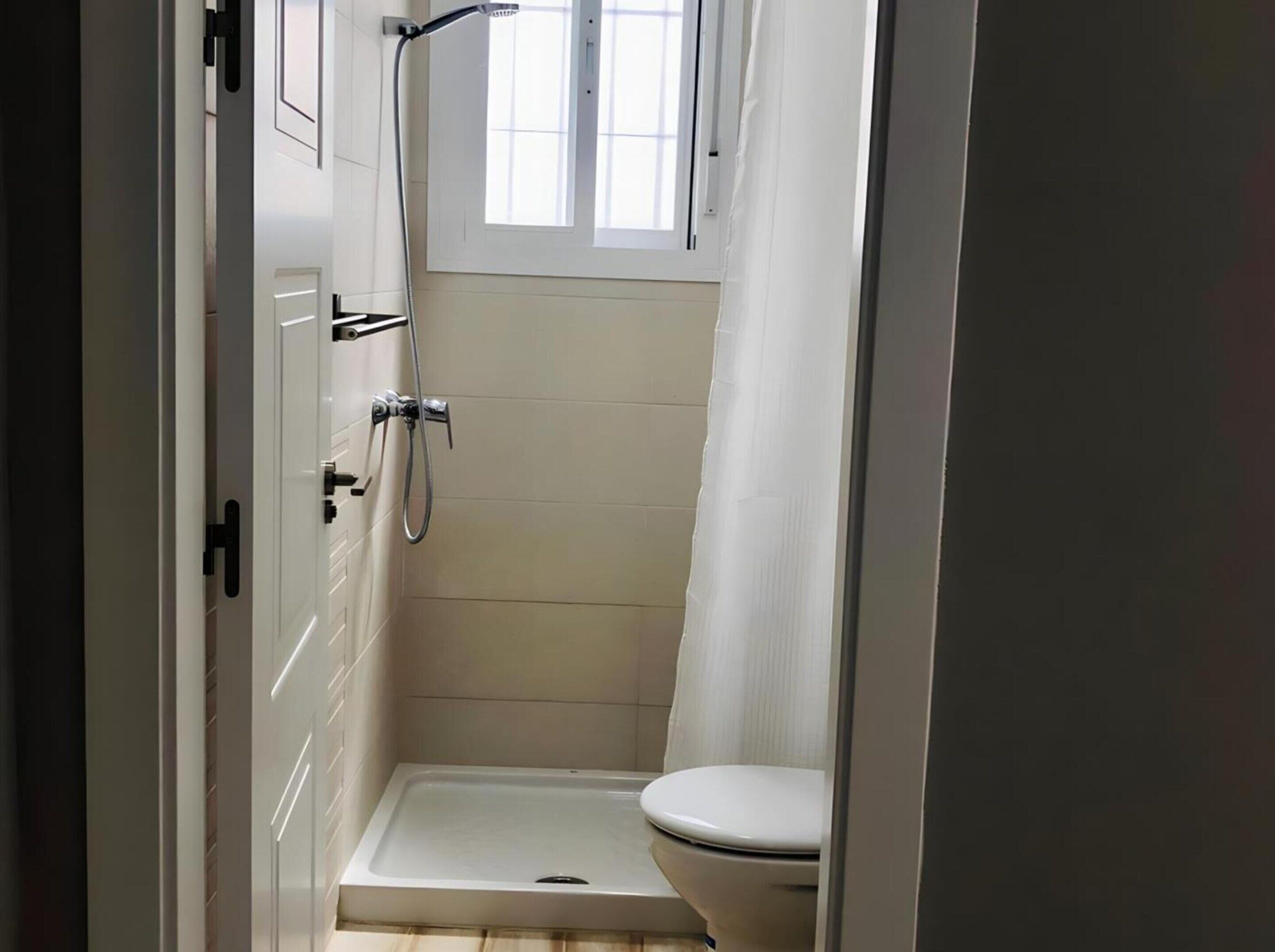 A small, enclosed bathroom with a shower, toilet, and a window.