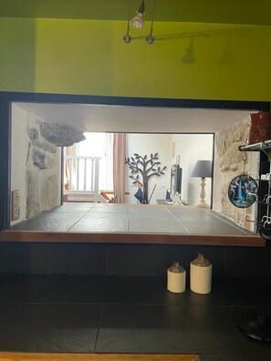 A room with a large window, a stone wall, a tree decoration, and a shelf with various items. - The Patou's house (Cadéac)