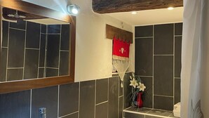 A bathroom with a white sink, a freestanding bathtub, dark tiled walls, and a wooden ceiling beam. - The Patou's house (Cadéac)