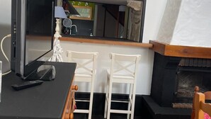 En hyggelig, kompakt opholdsstue med tv på et træbord, to hvide stole, et lille køkken og en pejs.