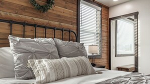 Ein ordentlich gemachtes Bett mit Kopfteil, einer Nachttischlampe und Blick auf ein Fenster mit Jalousien.
