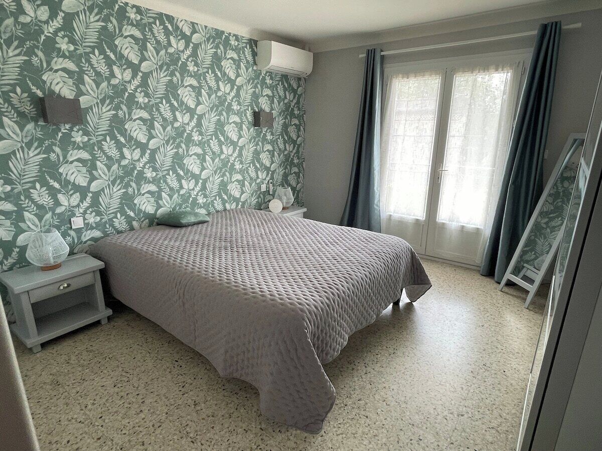 Una camera da letto con un letto, un comodino, un condizionatore fissato al muro e una finestra con tende.