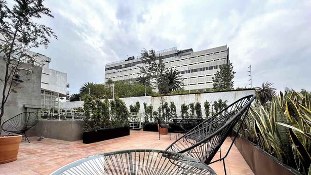 Una terrazza sul tetto con un'area salotto circolare, piante in vaso e un edificio moderno sullo sfondo.