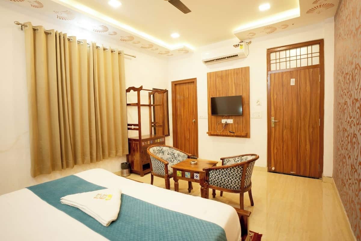 A hotel room with a bed, a desk with chairs, a TV, and wooden doors.