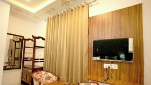 Une chambre d’hôtel avec un meuble en bois pour la télévision, un bureau, deux chaises, un miroir et un rideau.