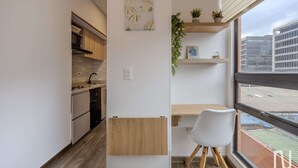Uma cozinha compacta com eletrodomésticos modernos, um espaço de jantar com vista e uma pequena planta no parapeito da janela.