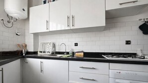 Moderni keittiö, jossa on valkoiset kaapit, musta työtaso ja sisäänrakennettu liesi.