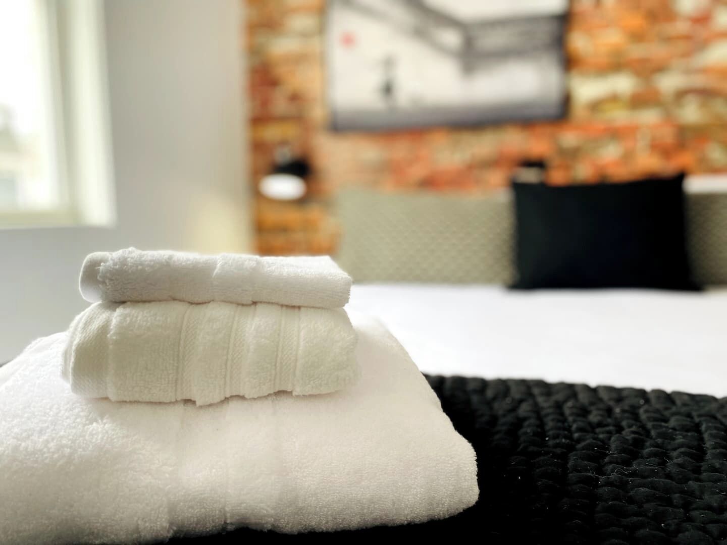 Cama bem arrumada com toalhas brancas e manta preta texturizada.