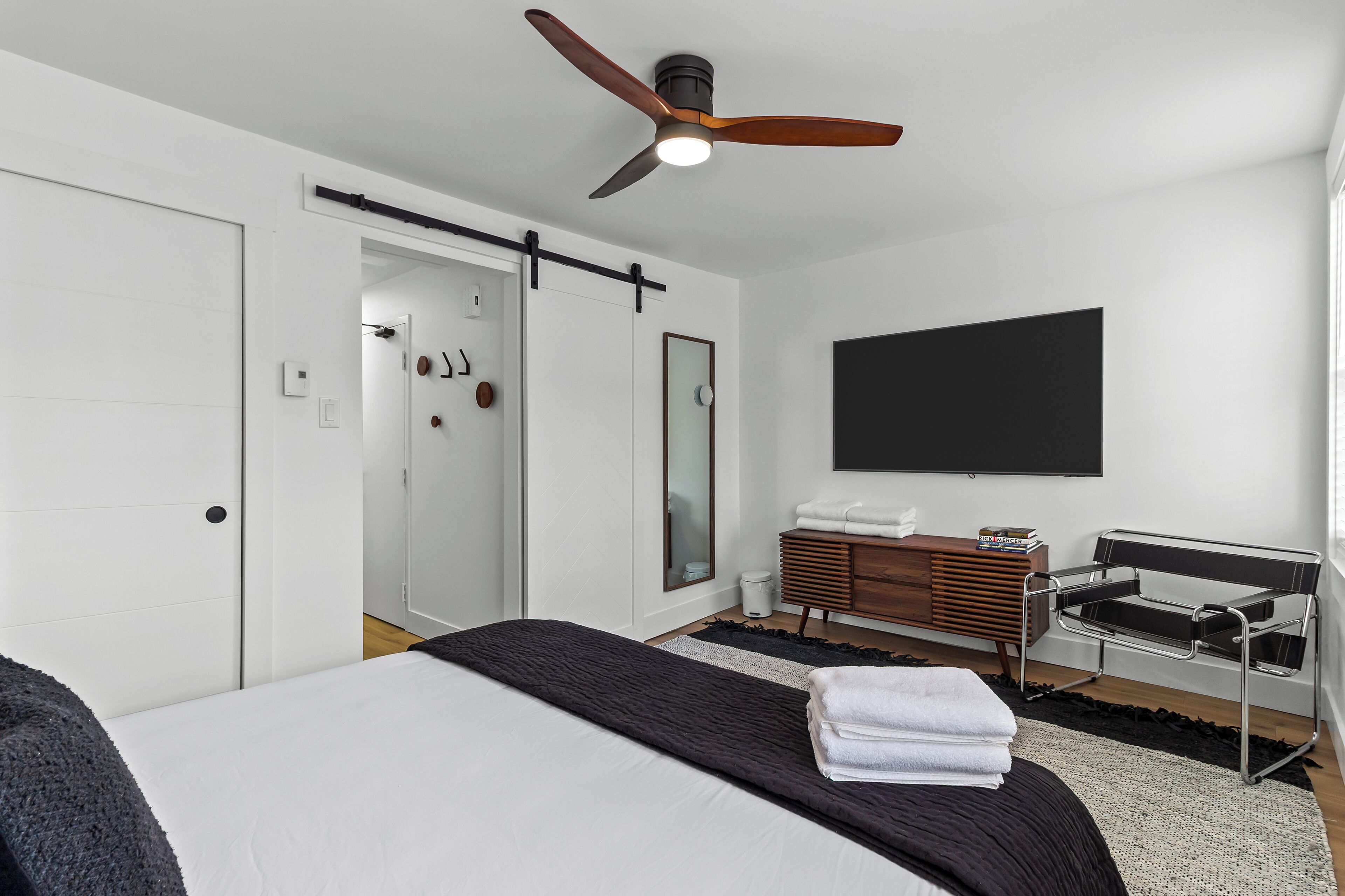 A modern bedroom with a bed, a ceiling fan, a TV, a dresser, and a sliding door.