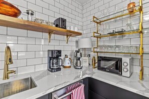 A modern kitchen with white tiled backsplash, a marble countertop, a built-in oven, a coffee maker, a kettle, and a shelf with glassware. - Gower Flat 2 Bed A/C with Patio, Signal Hill View (St. John's)