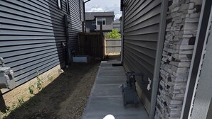 A narrow concrete pathway leading to a house with a wooden fence and a stone wall. - Cozy 1 bedroom Suite, Kitchenette & self check in (Edmonton)