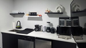 A compact kitchen with a dishwasher, coffee maker, blender, and a microwave. There are shelves with kitchen essentials and a refrigerator. - Cozy 1 bedroom Suite, Kitchenette & self check in (Edmonton)