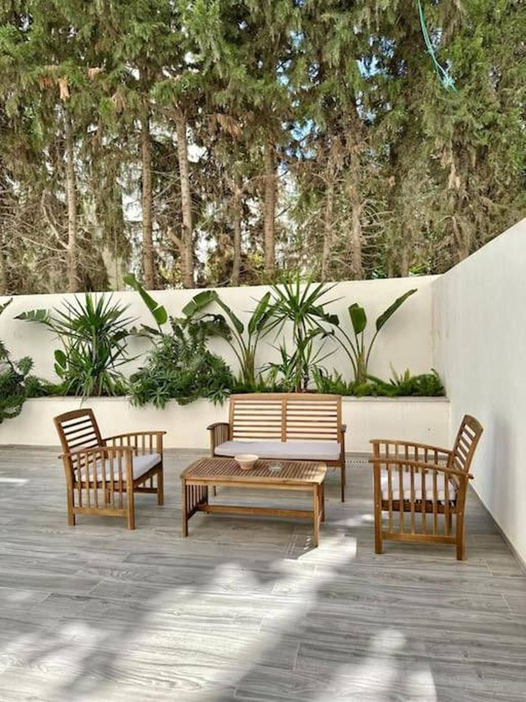 An outdoor seating area with a wooden table and chairs, surrounded by lush greenery and tall trees.