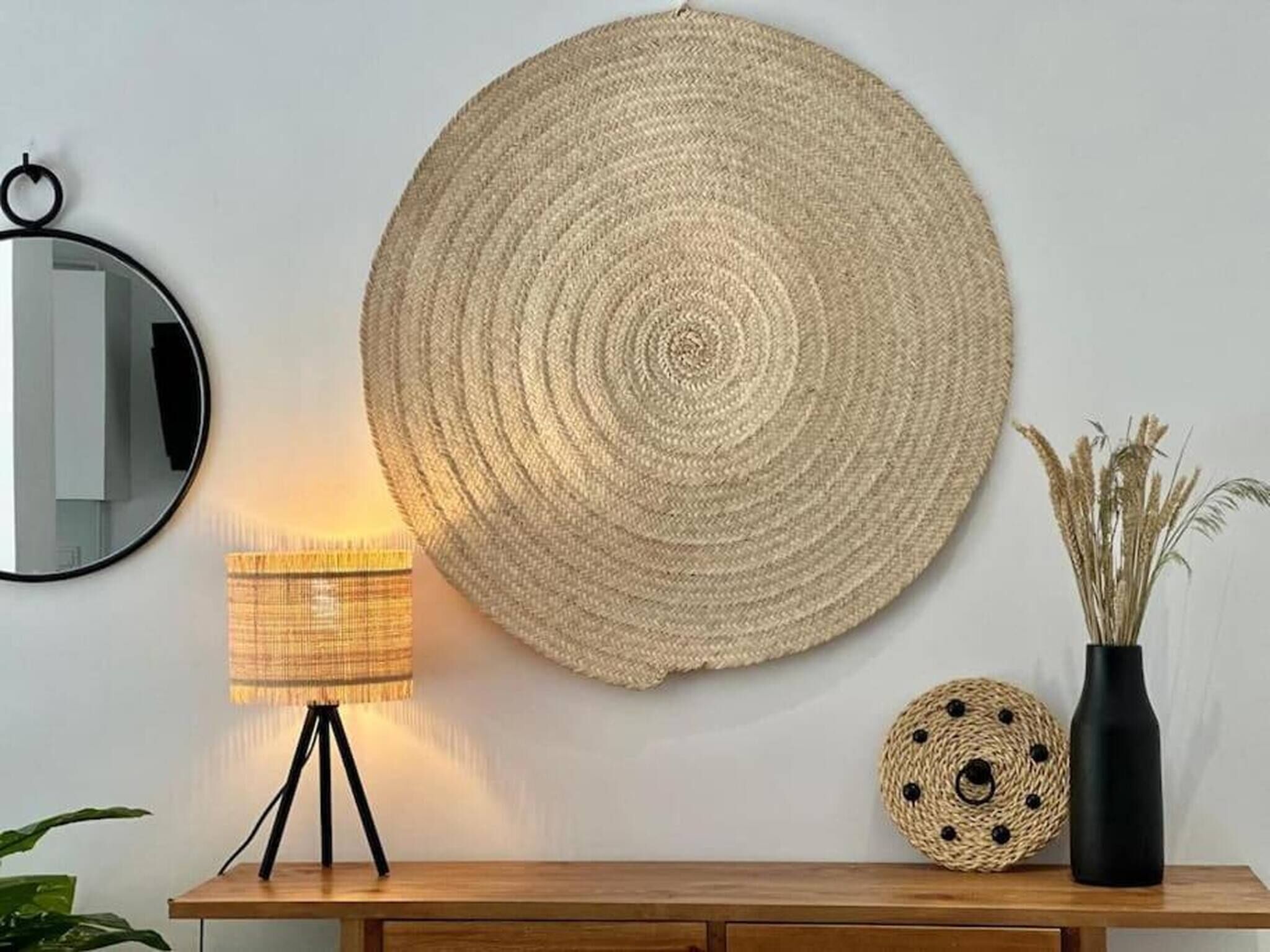 A round woven wall hanging, a lamp, and decorative items on a wooden console table.