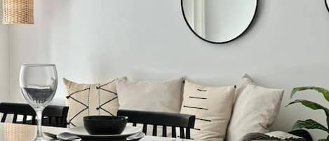 En matplats med ett vitt bord, svarta stolar, en flätad hänglampa och en vägg med tre runda speglar.
