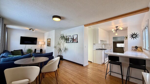 Una sala de estar moderna con un sofá azul, una mesa de comedor redonda y una zona de cocina con armarios blancos y una estufa.