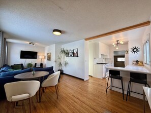 A modern living room with a blue sofa, a round dining table, and a kitchen area with white cabinets and a stove. - Cozy 3bd King Ed Near Whyte Ave (Edmonton)