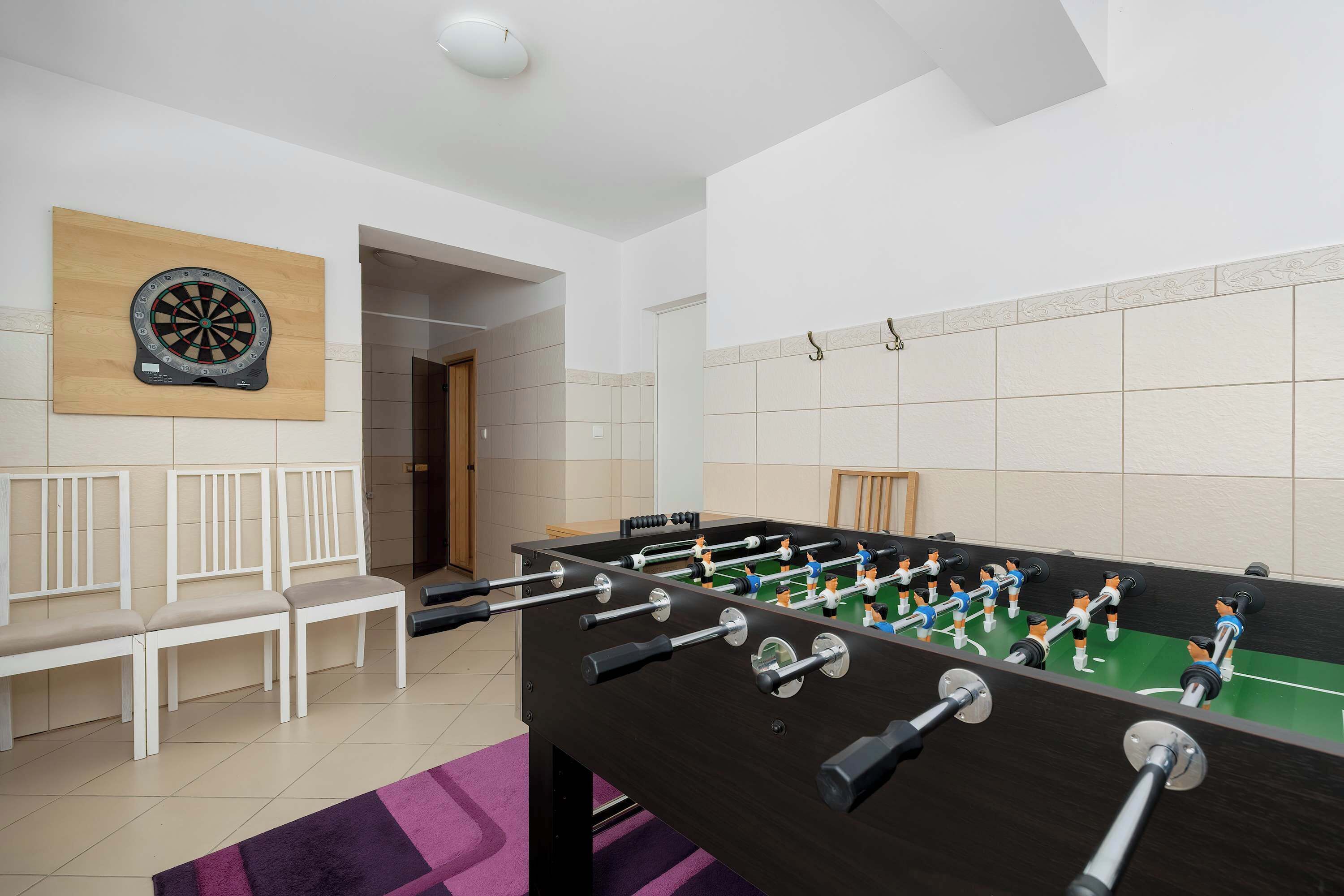 Une pièce équipée d’un baby-foot, d’un jeu de fléchettes et d’un espace détente avec des fauteuils.