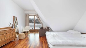 Een slaapkamer met een houten dressoir, een grijze bank, een bed met witte lakens en uitzicht op een besneeerd landschap door een raam.