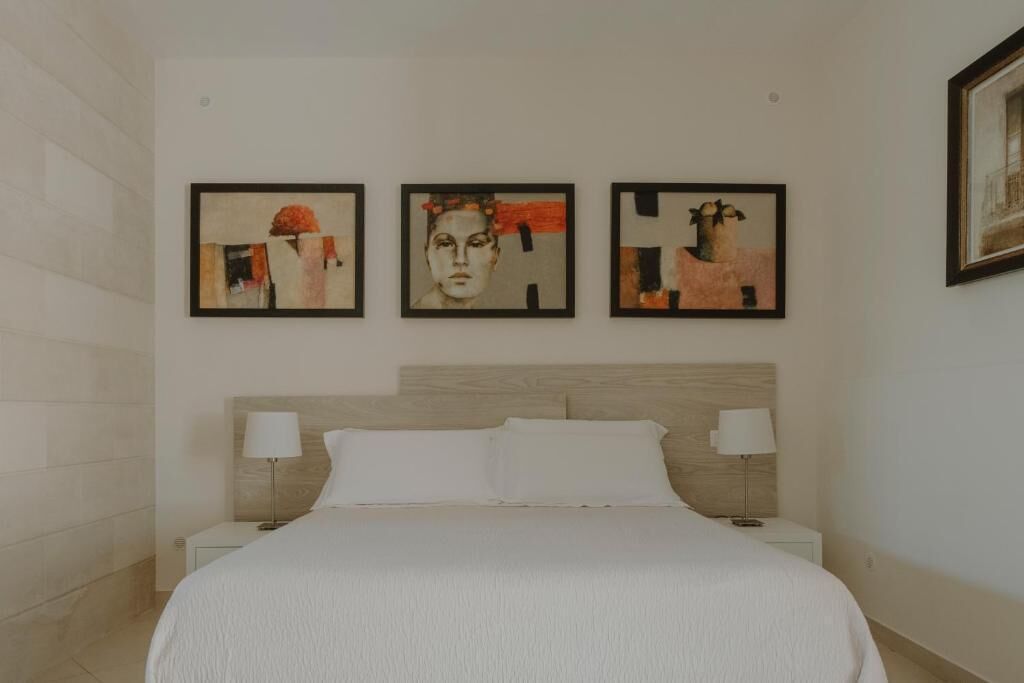 A hotel room with a large bed, two bedside tables with lamps, and three framed artworks on the wall.