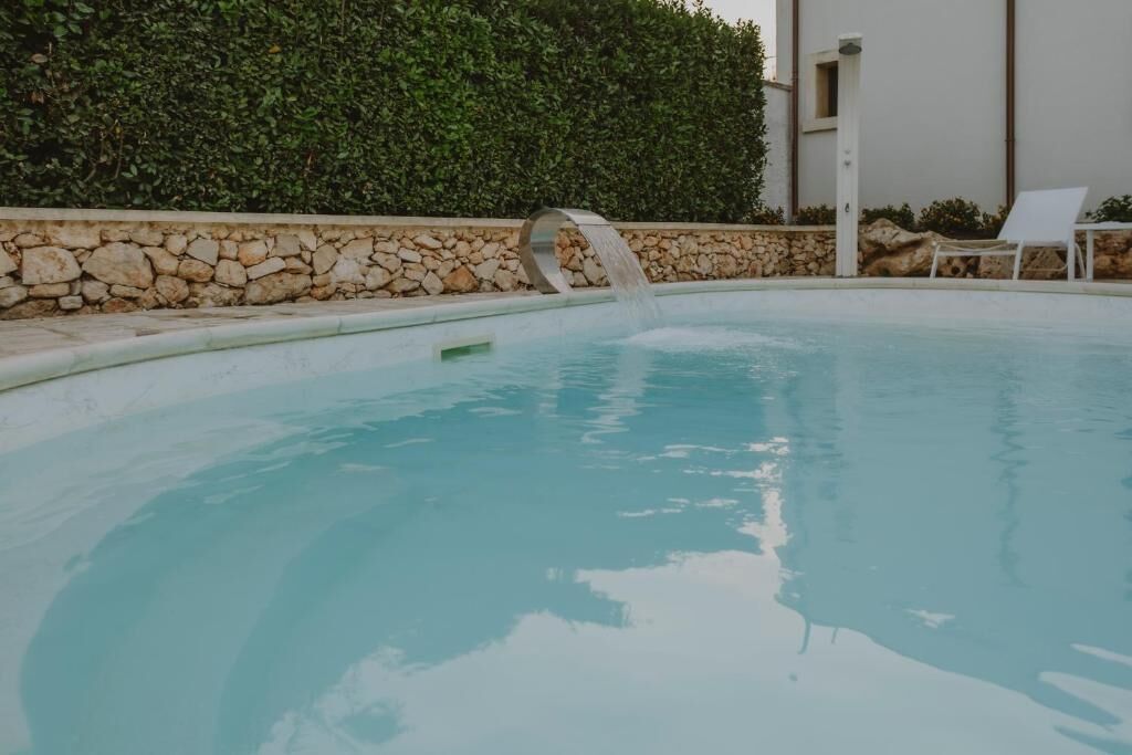 Una piscina con un muro de piedra y un edificio blanco al fondo.