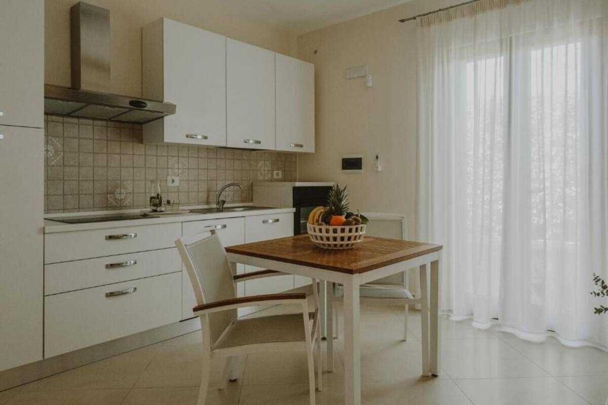A modern kitchen with white cabinets, a wooden table, and a bowl of fruit.
